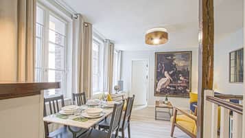 A dining area with a table set for four, a globe, and a bottle on the table. There is a large painting on the wall and a staircase to the right.