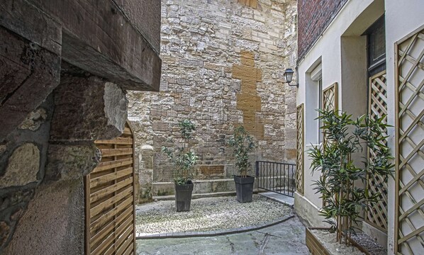A narrow alley with stone walls, a wooden gate, and potted plants.