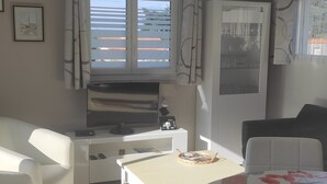 A modern room with a dining table, chairs, a TV, and a window with curtains. - Bungalow (BREM SUR MER)