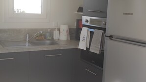 A compact kitchen with dark cabinets, a sink, a stove, and a refrigerator. - Bungalow (BREM SUR MER)
