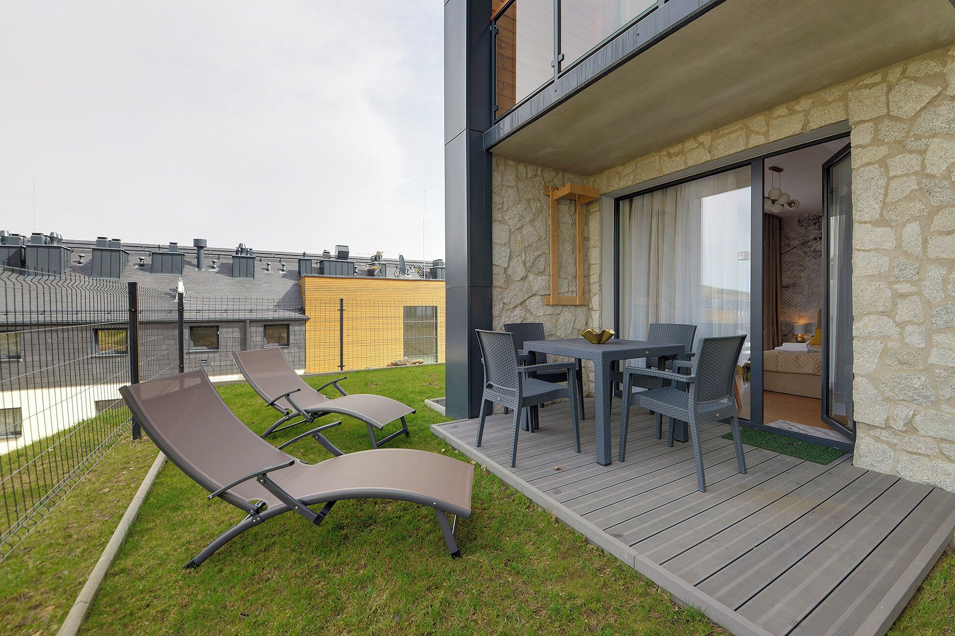 Un balcone con tavolo e sedie, una poltrona relax e un muro in pietra.