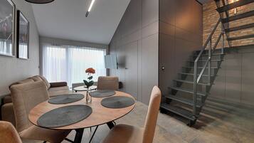 Un espace de salle à manger moderne avec une table ronde, des chaises rembourrées et un escalier doté d’une rampe en métal.