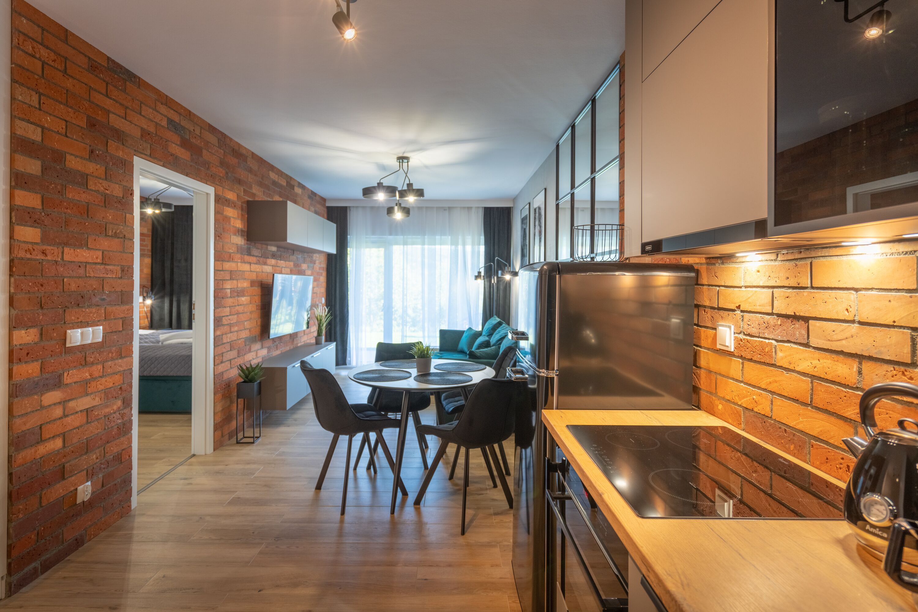 A modern kitchen with a brick wall, wooden countertop, and a kettle.