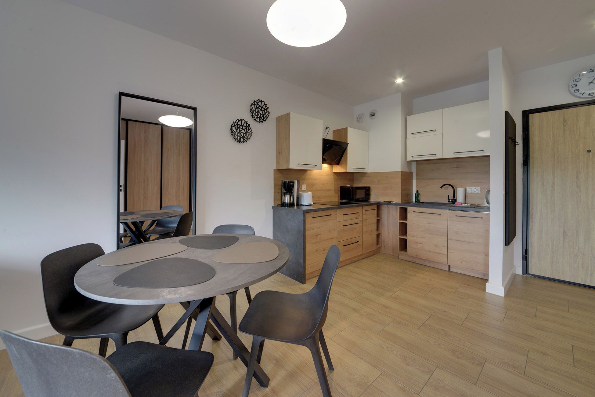 A modern kitchen with wooden cabinets, a microwave, and a coffee maker. There is a dining area with a round table and chairs.