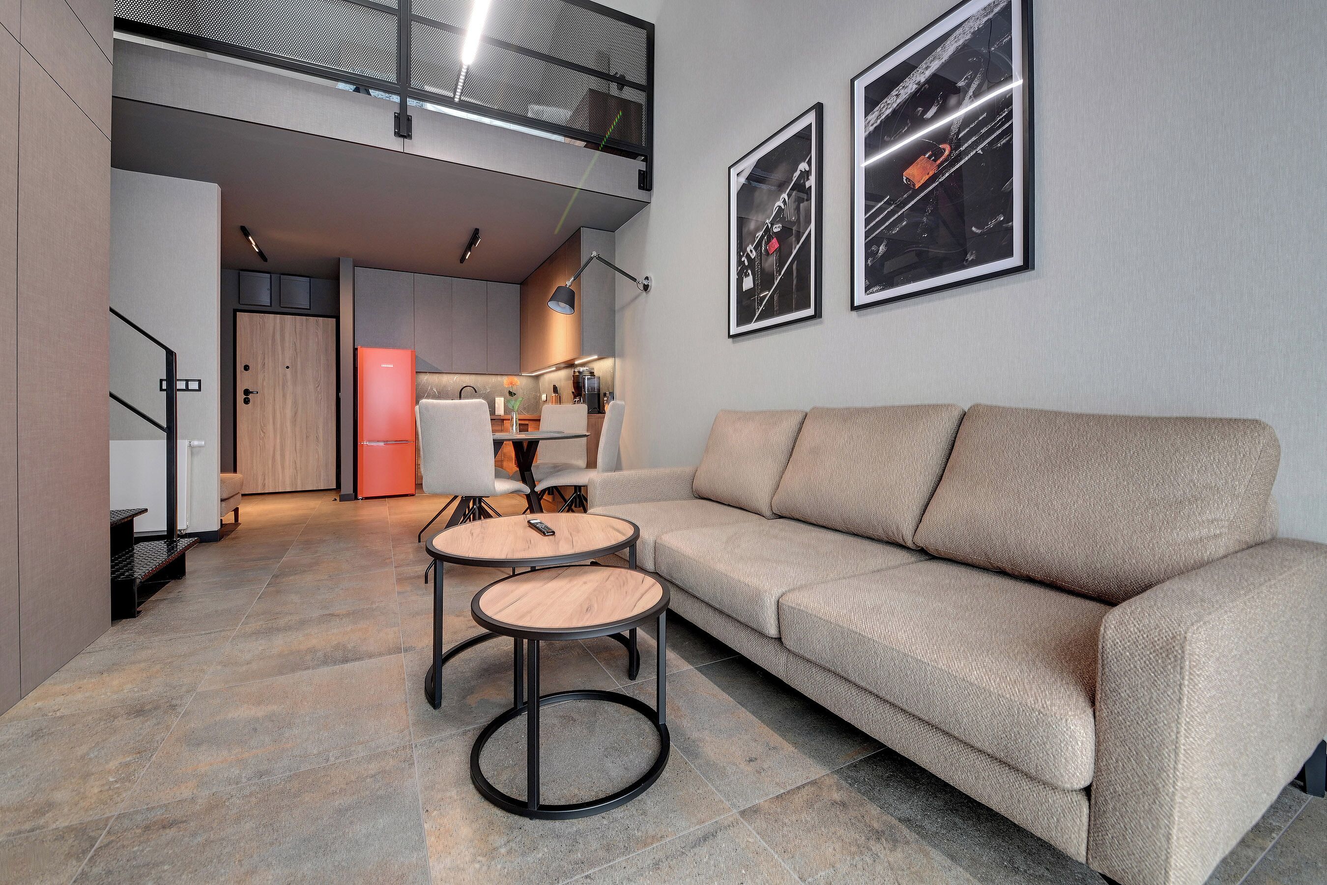 Ein modernes Wohnzimmer mit einer Couch, zwei runden Tischen, einer Küche im Hintergrund und zwei gerahmten Bildern an der Wand.