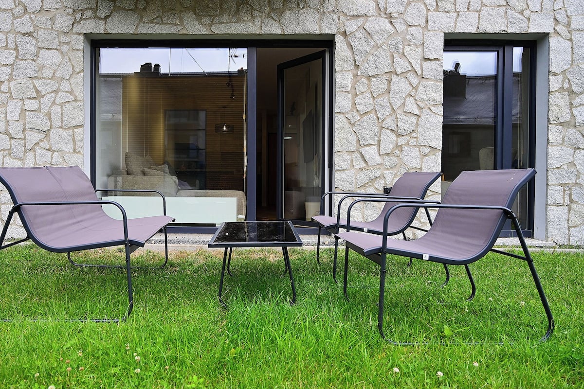 Un espace extérieur aménagé avec quatre chaises et une table, situé devant un bâtiment en pierre doté de grandes portes vitrées.