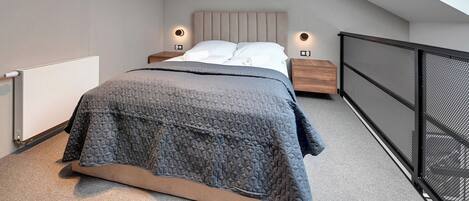 A bedroom with a bed, nightstands, a radiator, a window, and a balcony railing.