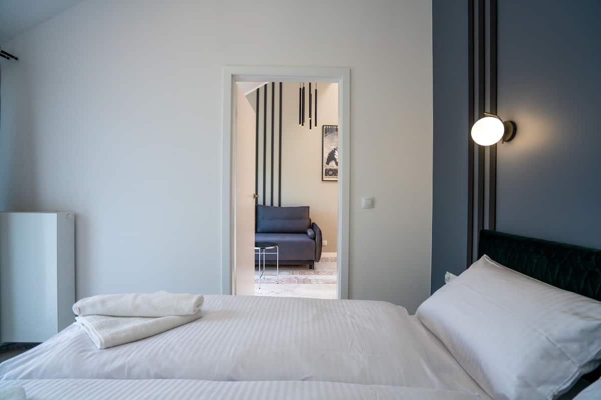 Une chambre d’hôtel avec un lit bien fait, un canapé en arrière-plan et un luminaire fixé au mur.