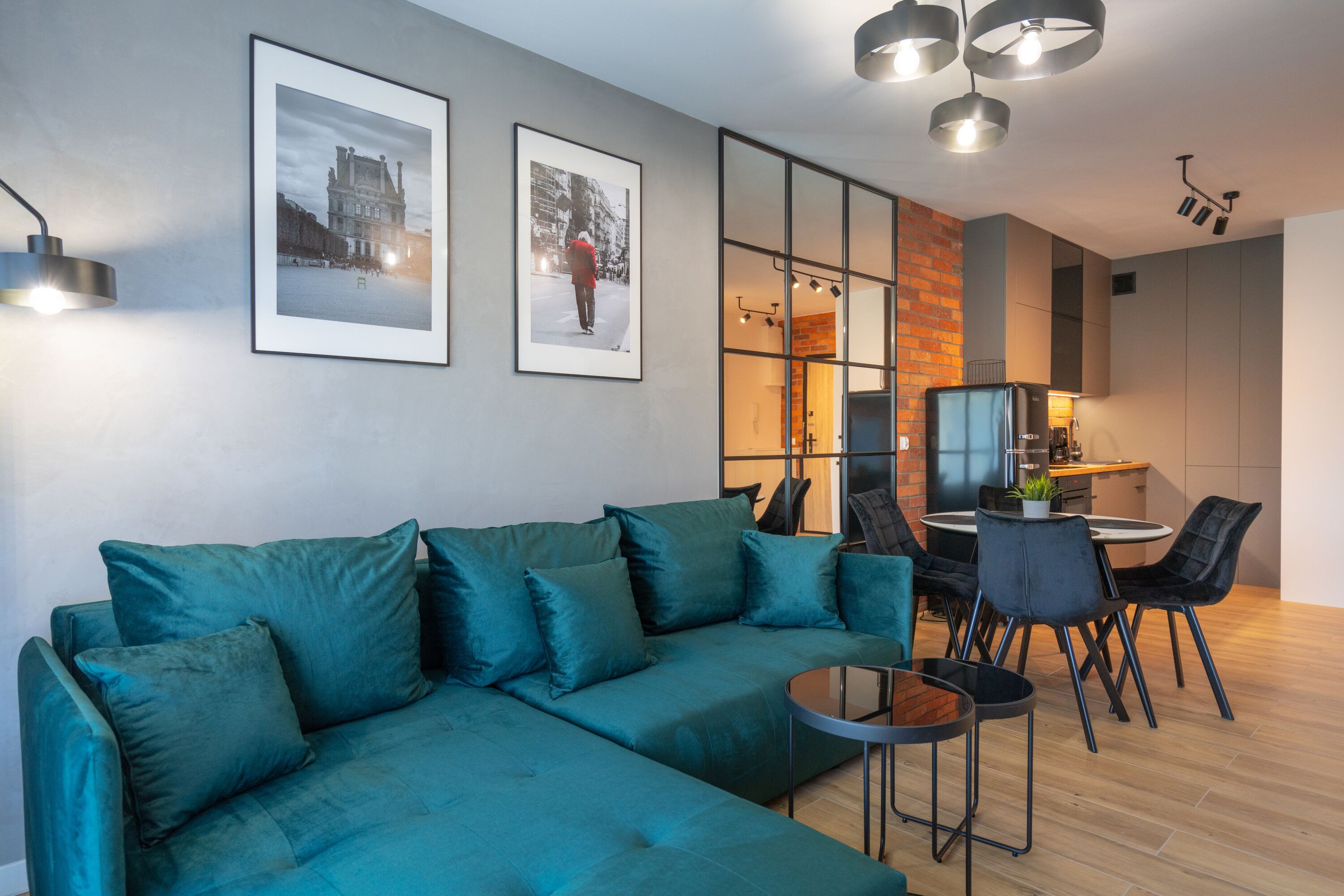 Un salon moderne avec un canapé de couleur turquoise, une table à manger avec des chaises et un coin cuisine visible à travers une cloison en verre.