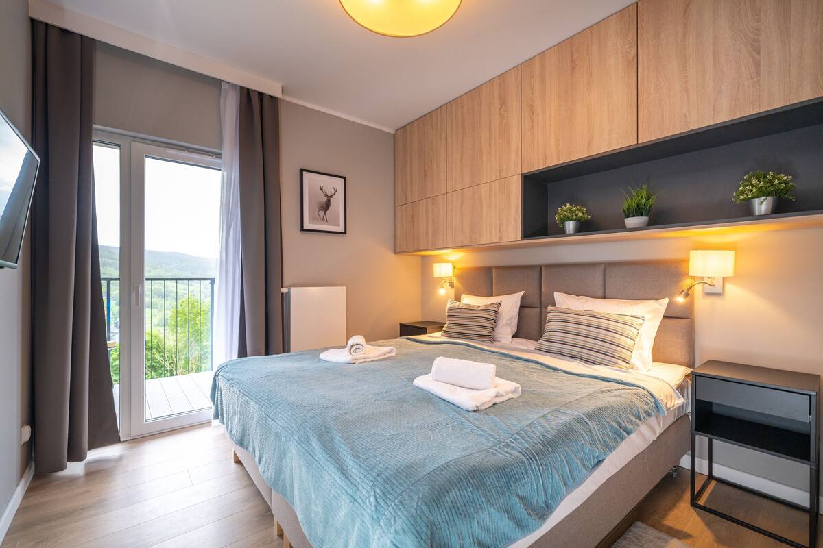 Une chambre moderne avec un grand lit, des lampes de chevet, une télévision et un balcon agrémenté de rideaux.