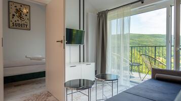 Habitación de hotel moderna con cama, televisión, una mesita y balcón con vistas al bosque.