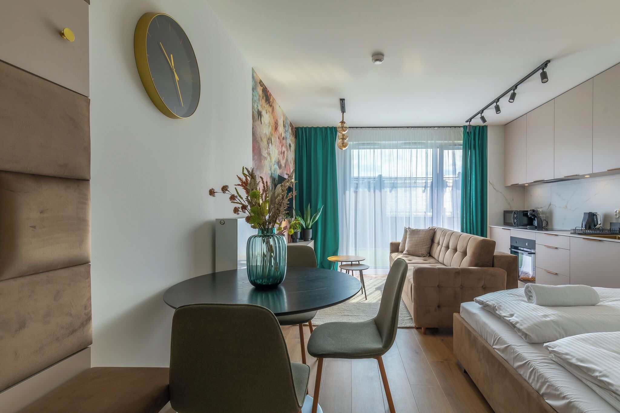 Een moderne hotelkamer met een ronde eettafel, een bank, een bed en een keukenhoek.