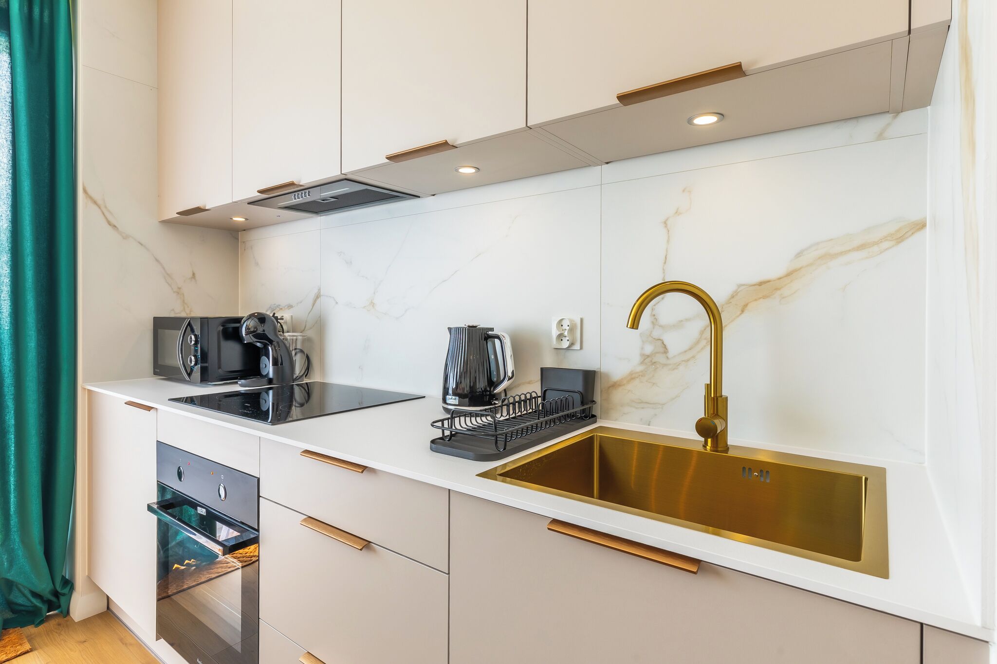 A modern kitchen with a built-in oven, a coffee maker, and a gold-colored sink.