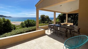 A covered outdoor area with a table and chairs, overlooking a beach and the sea. - House (Calcatoggio)