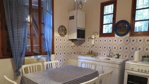 A kitchen with a checkered tablecloth, white chairs, a stove, and a window with curtains. - House (Calcatoggio)