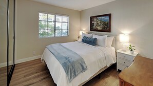 Un dormitorio con cama, mesitas de noche, un cuadro y una ventana con persianas.