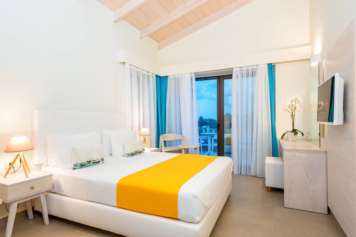 A modern hotel room with a large bed, a desk, a chair, and a TV.