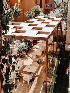 An outdoor seating area with tables and chairs under a wooden pergola, surrounded by potted plants and flowers. - Airis Boutique & Suites (Chania)