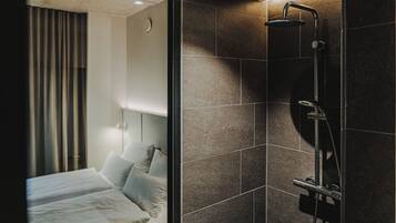 A modern hotel room with a large bed, a shower area, and a view of the cityscape.