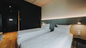 Ein Hotelzimmer mit zwei Betten, Holzboden, dunkler Wand und heller Decke.