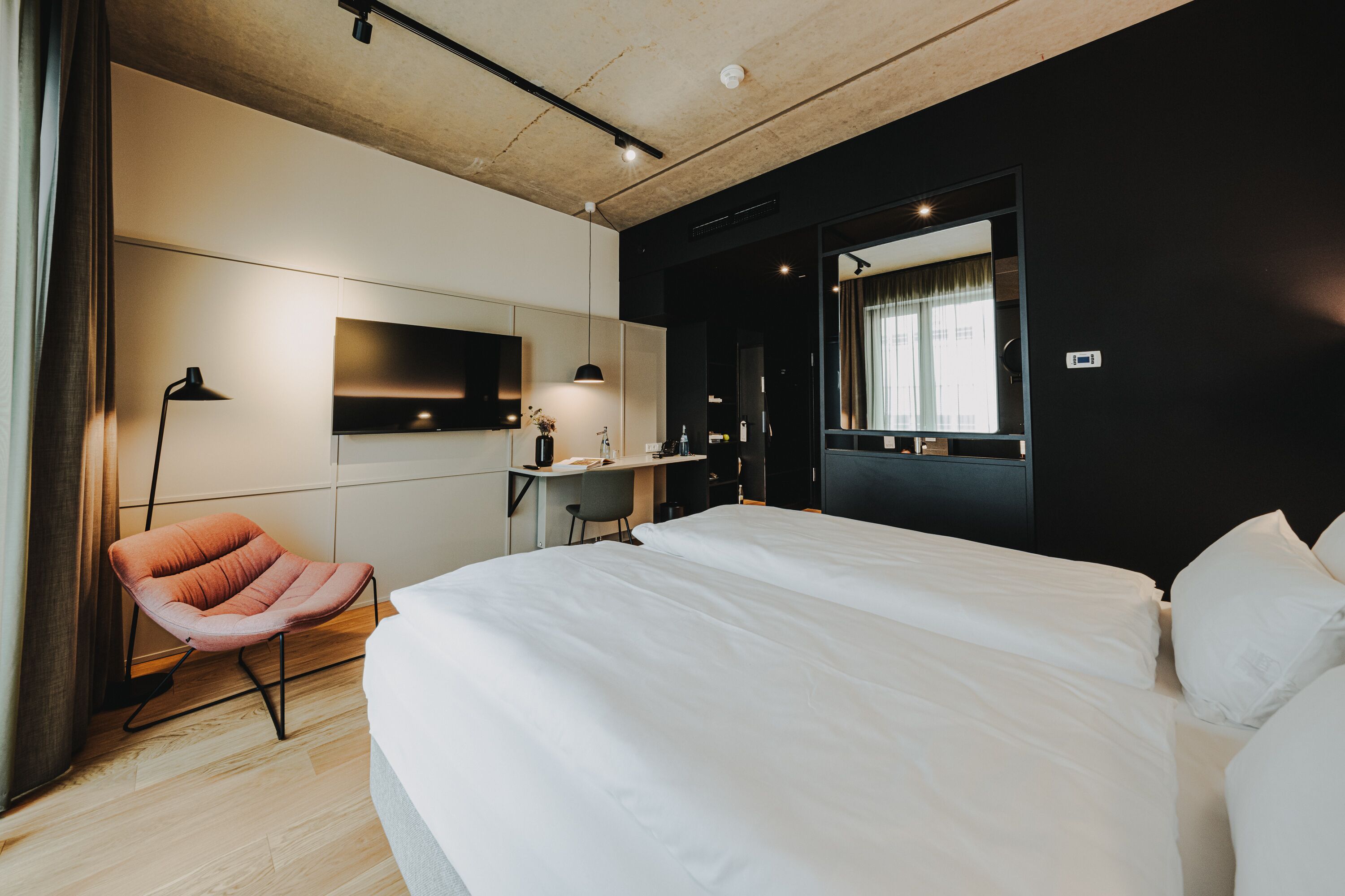 A modern hotel room with a large bed, a desk with a chair, a flat-screen TV, and a large mirror.