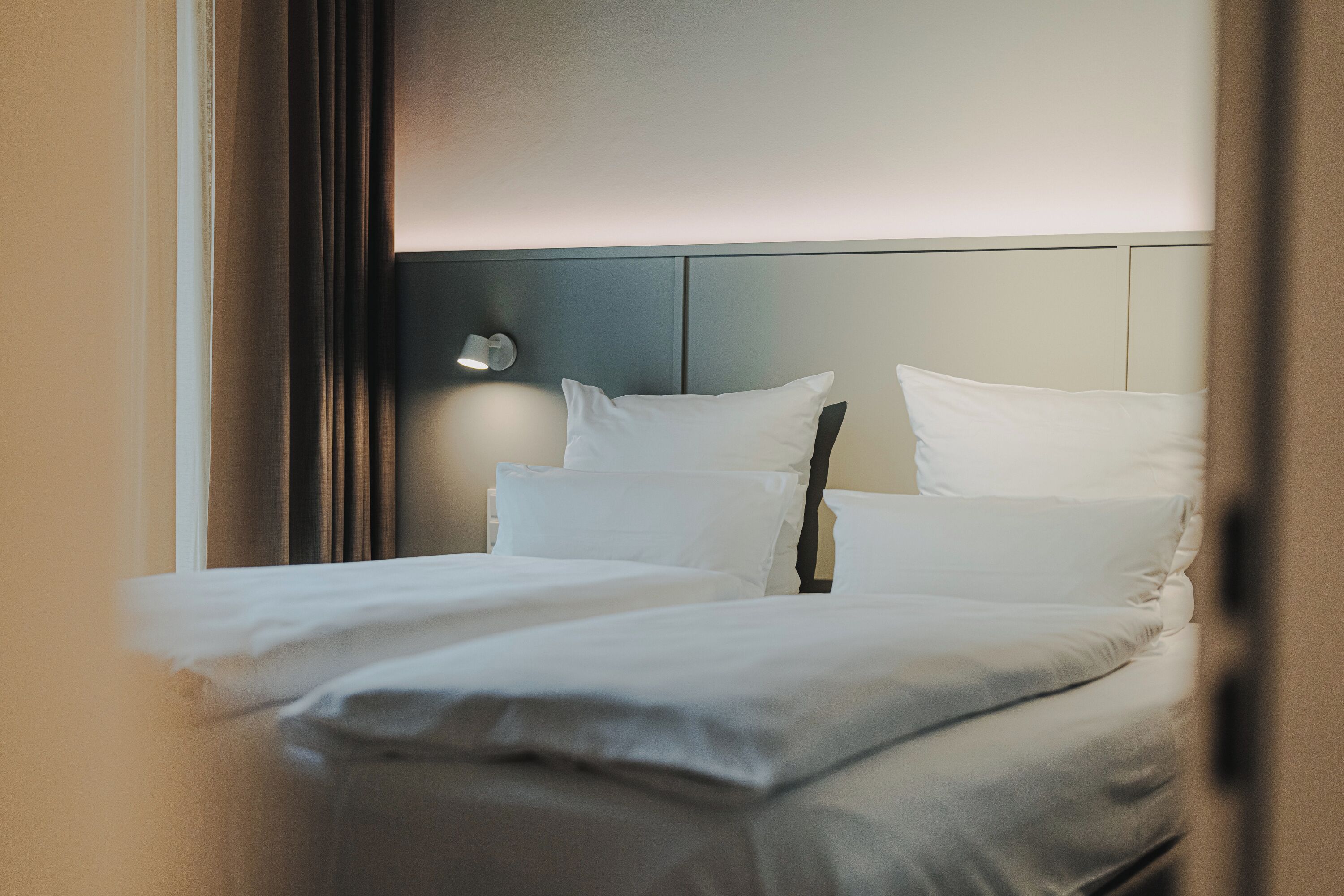 A neatly made bed with white linens and a headboard with a light fixture.