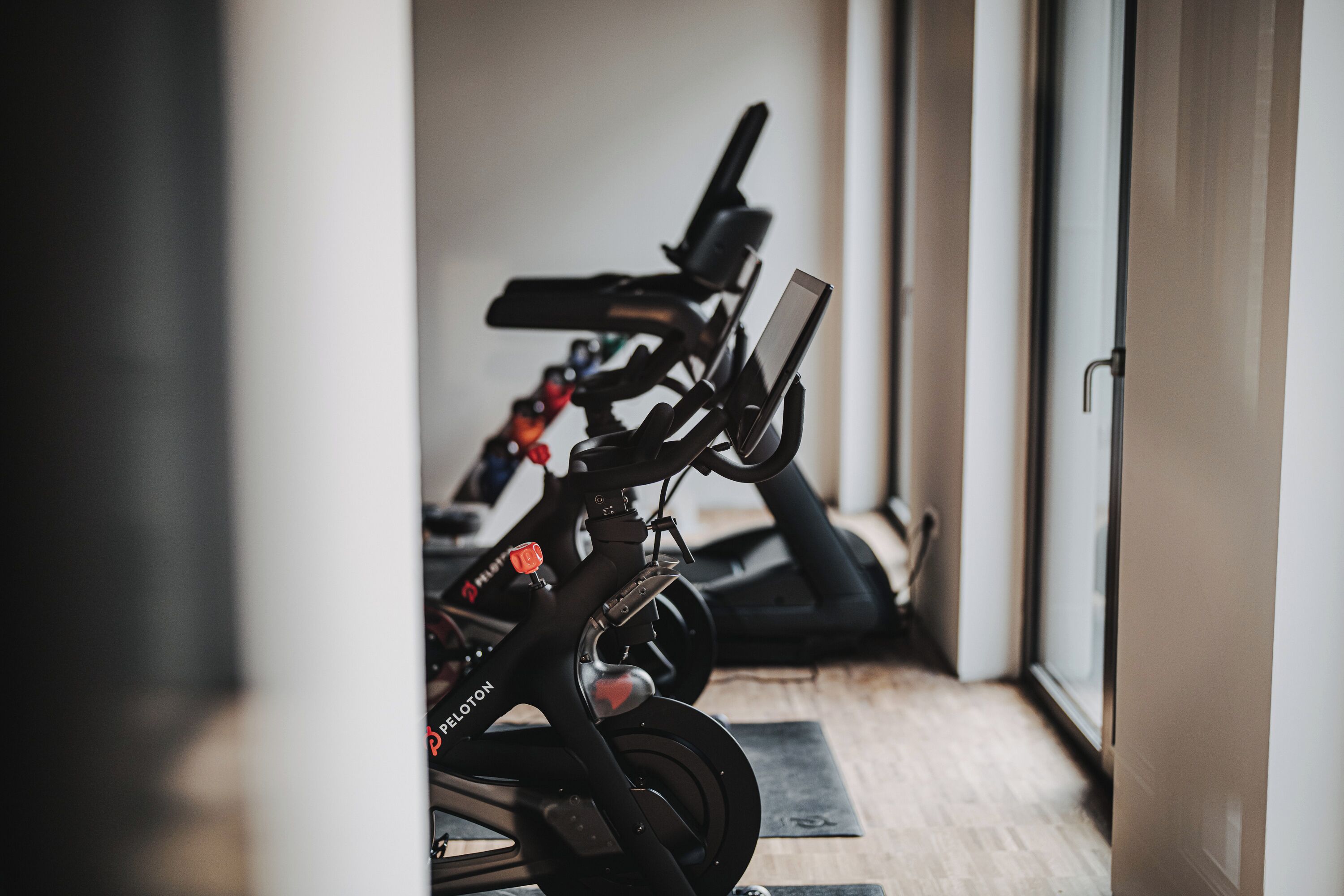 A row of stationary bikes in a room with a wooden floor and a door on the right.