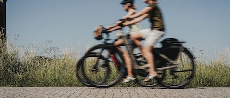 Dos personas andando en bicicleta por un camino pavimentado, con césped a ambos lados.