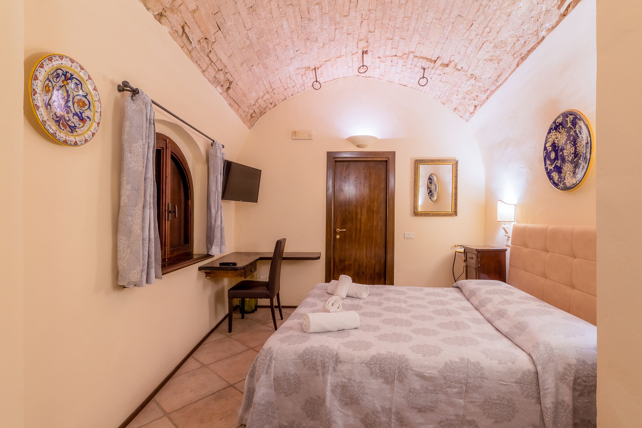 A bedroom with a bed, a desk, a chair, a TV, and a door.