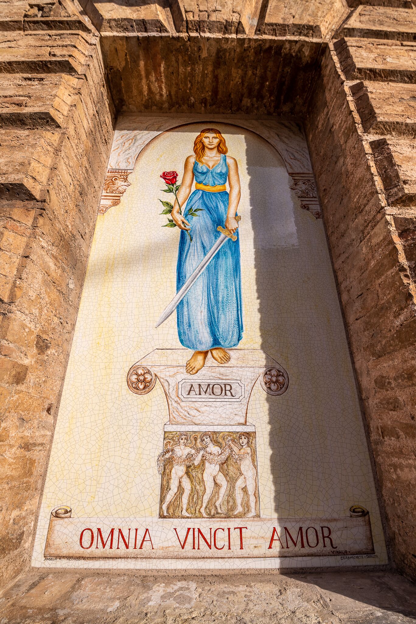 Un mosaico raffigura una donna che tiene una spada e una rosa, con le scritte “AMOR” e “OMNIA VINCIT AMOR”.