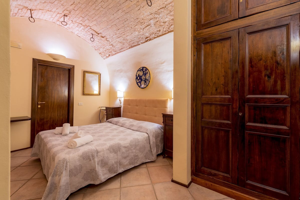 A bedroom with a bed, wooden wardrobe, and a decorative plate on the wall.