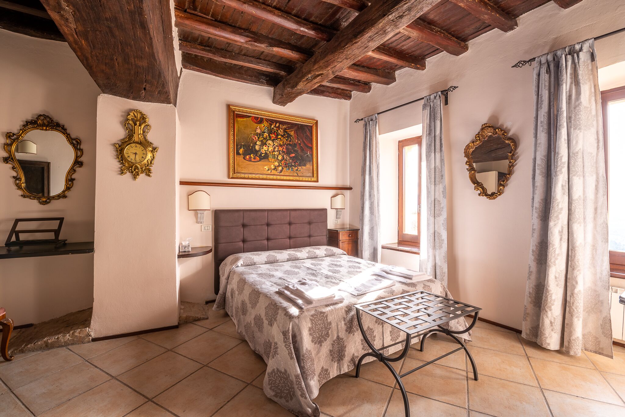 Quarto com cama, mesa de cabeceira, espelho, quadro e janela com cortinas.