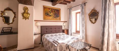 A bedroom with a bed, a nightstand, a mirror, a painting, and a window with curtains.