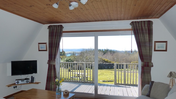 Una sala de estar con televisor, radio y una mesa con flores. Hay un balcón con vistas al exterior.