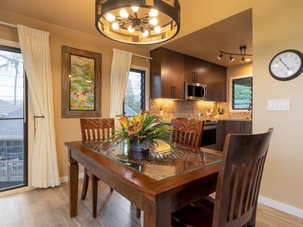 A dining area with a glass table, wooden chairs, and a potted plant.