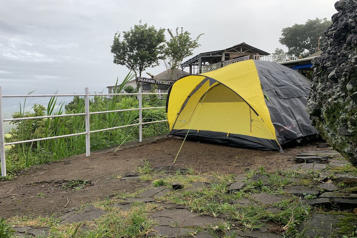 A yellow and black tent set up on a rocky terrain with a view of a building in the background.