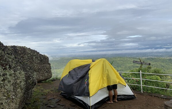 A tent set up on a rocky outcrop with a view of a valley and a sign reading "DILARANG TERJUN". - Camping Ground Watu Amben (Srimulyo)