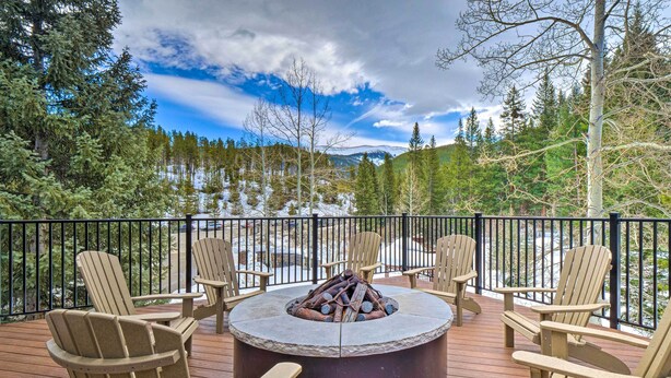 A deck with a circular fire pit surrounded by Adirondack chairs, overlooking a snowy landscape with trees and mountains. - Chic Winter Park Studio w/ Community Hot Tub (Winter Park)