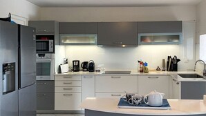 A modern kitchen with grey cabinets, a built-in oven, a coffee maker, and a kettle on the counter. - LA Maison DES Fées (Les Trois-Îlets)