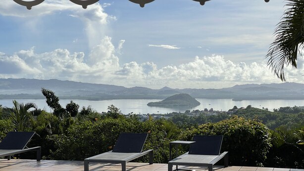 A poolside area with lounge chairs and a view of a lake and distant mountains. - LA Maison DES Fées (Les Trois-Îlets)