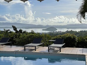 A poolside area with lounge chairs and a view of a lake and distant mountains.