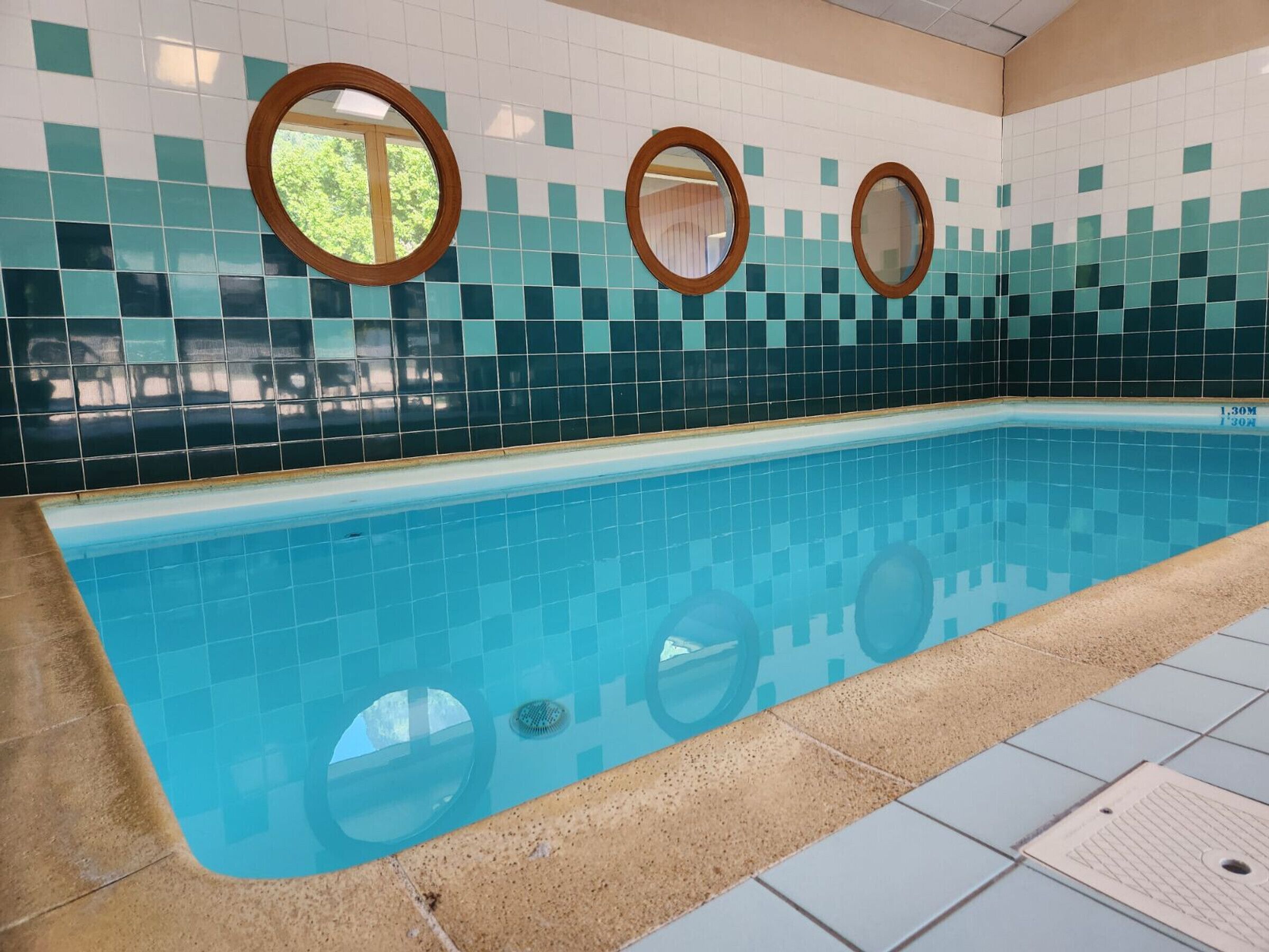 A swimming pool with tiled walls and three circular mirrors.