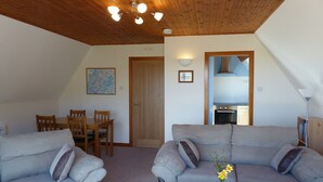 Ein gemütliches Wohnzimmer mit Holzboden, ein Essbereich mit Holztischen und -stühlen, und eine durchgehende Küche.