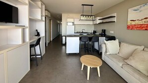 Une cuisine moderne dotée d’un îlot central, d’un coin repas avec des chaises, d’un canapé et d’un téléviseur fixé au mur.