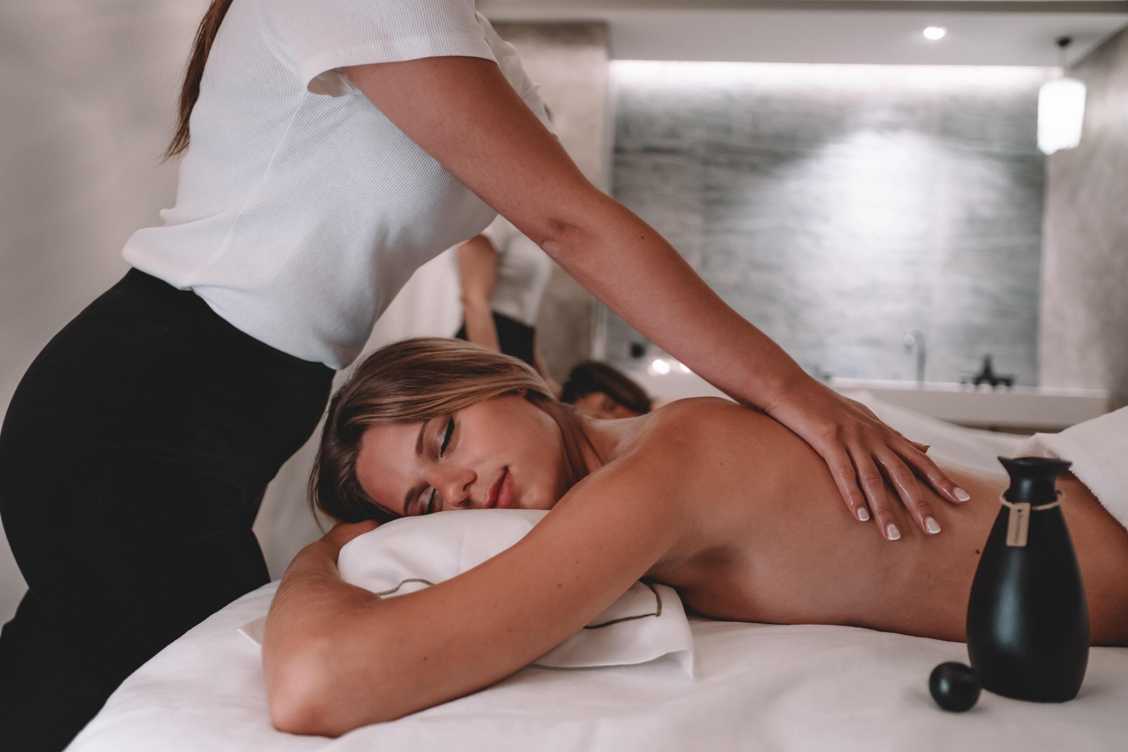 Une séance de massage thérapeutique dans un spa, avec une table de massage, un massothérapeute et une bouteille noire, qui contient probablement de l’huile ou une lotion.