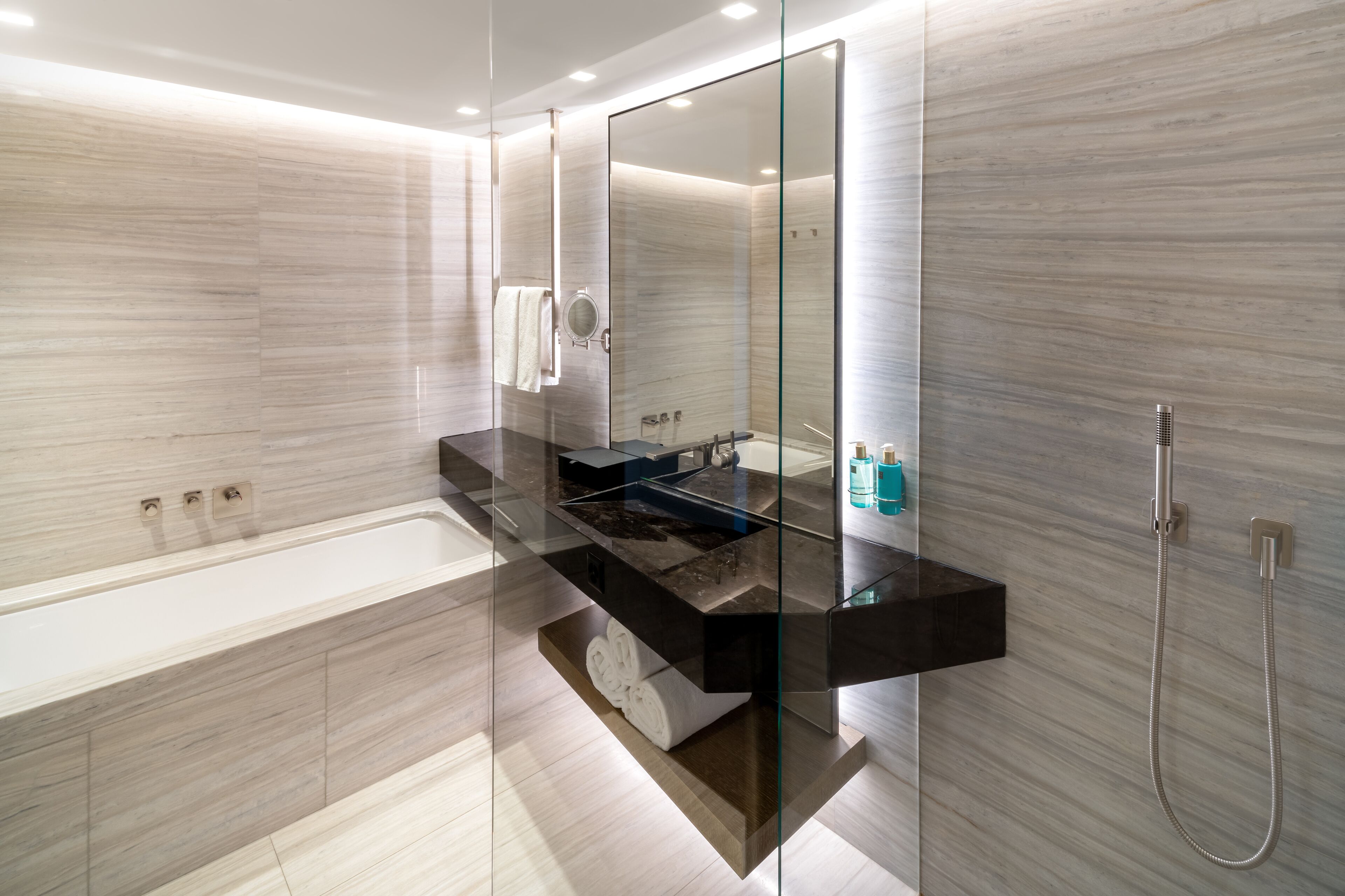 A modern bathroom with a glass-enclosed shower, a black countertop, and a large mirror.
