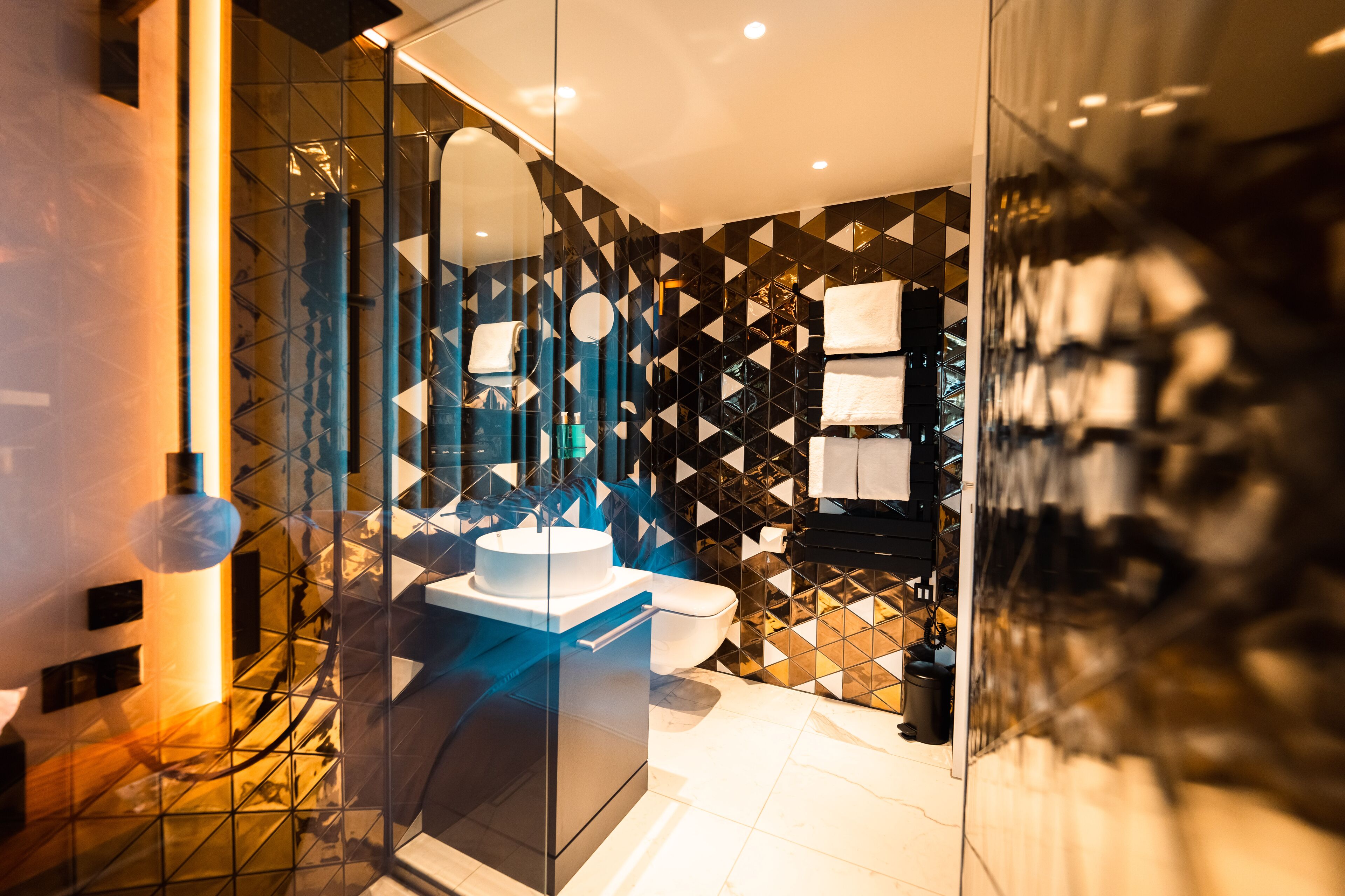Un bagno moderno con un box doccia in vetro, un lavandino bianco e una parete con decorazioni bianco e nero.