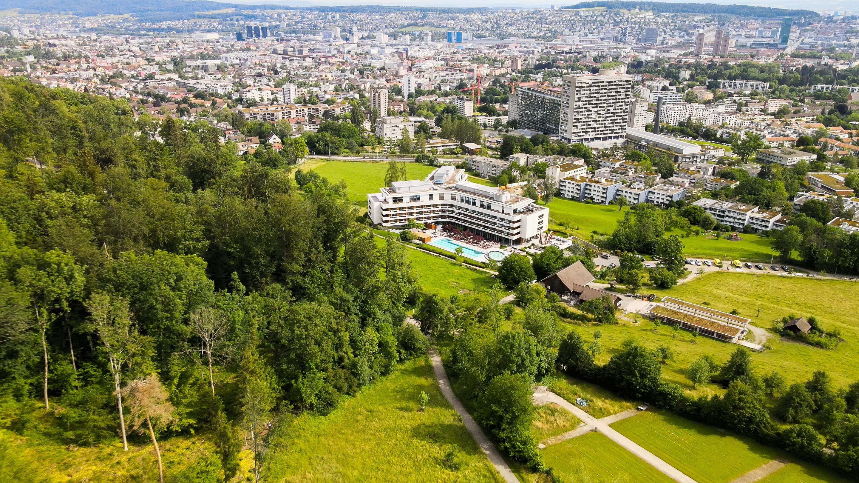 Un hotel con piscina, rodeado de vegetación y edificios urbanos.