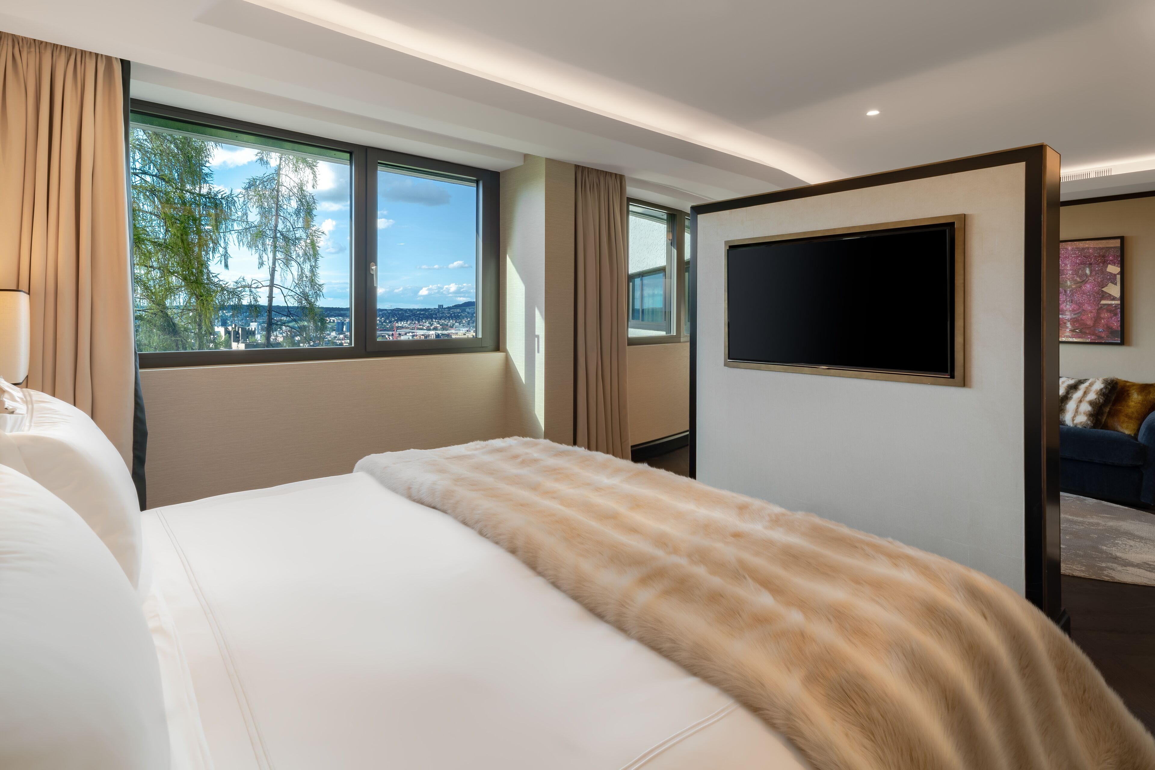 Una habitación de hotel moderna con una cama grande, un televisor de pantalla plana montado en la pared y una ventana con vistas a la ciudad.