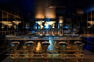 Um bar com um mapa-múndi ao fundo, banquetas e diversas garrafas.